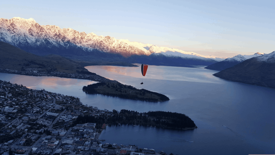 Paraglider soaring over Queenstown and Lake Wakatipu with the Remarkables mountain range at sunset — iconic New Zealand incentive travel and DMC destination experience